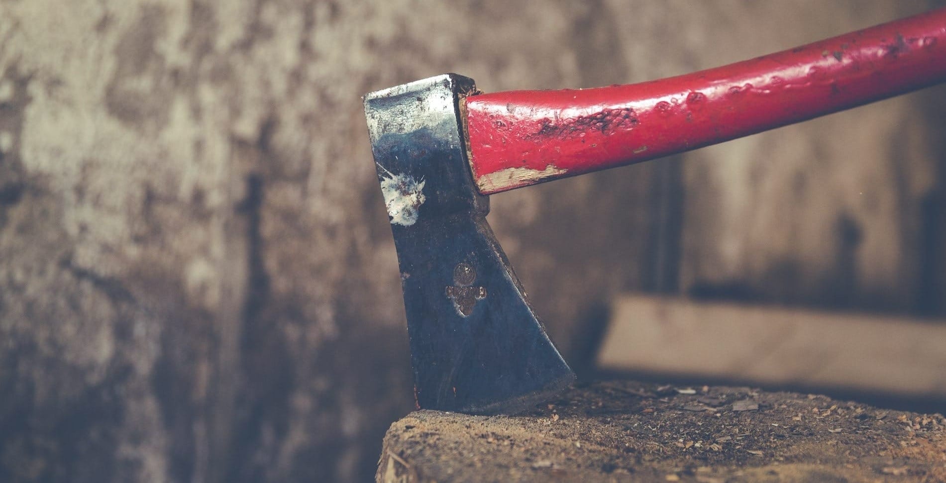 A dirty axe with a red handle bites into a round.